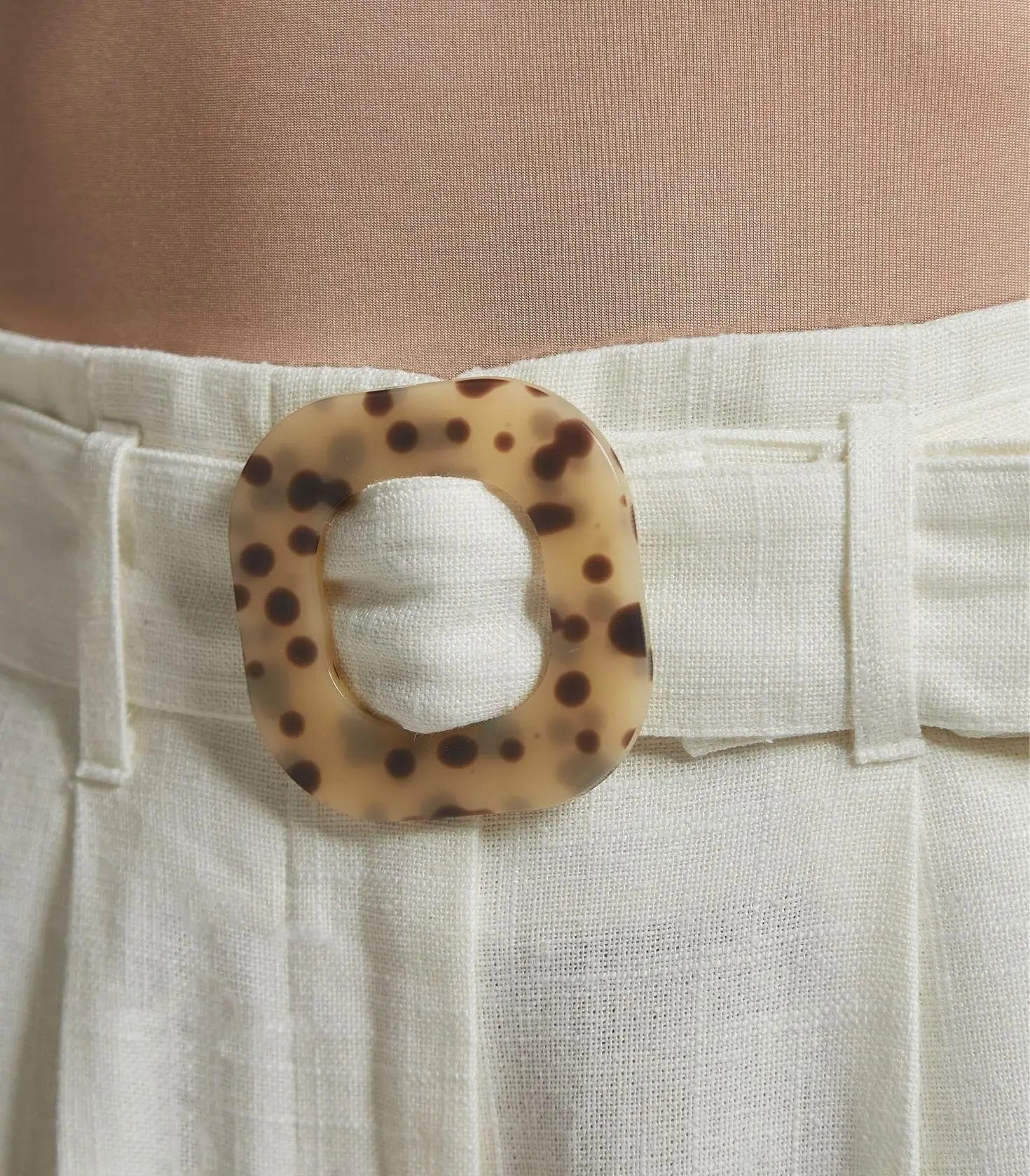 White pants with a leopard print belt buckle worn by a person.