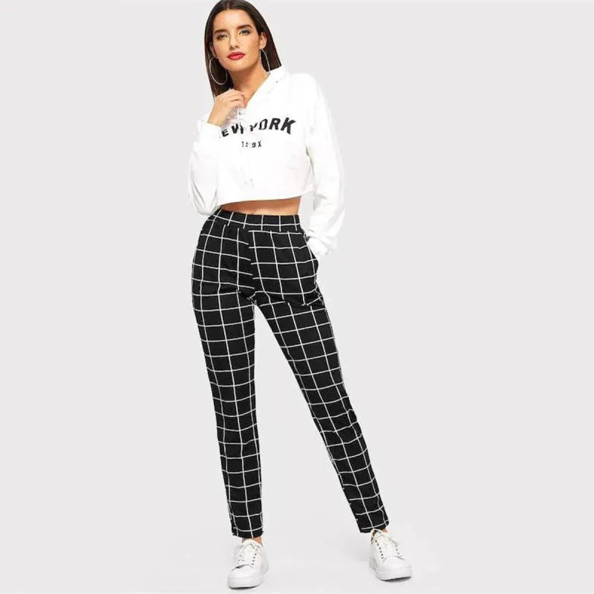 Woman wearing a white cropped sweatshirt and black plaid pants on a light gray background