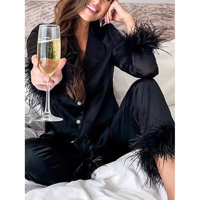Woman in black pajama set with feather details holding a glass of champagne.