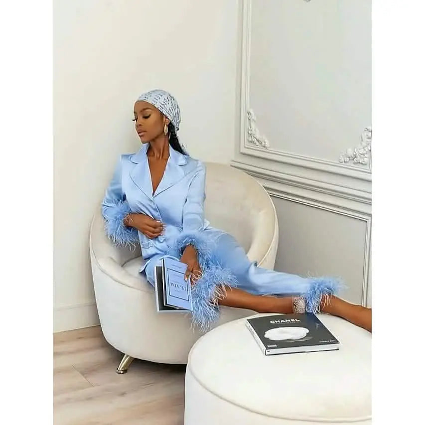 Woman in a light blue outfit with feather details sitting on a white chair in a stylish room.