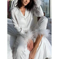 Person wearing a white outfit with feathered sleeves sitting on a bed.